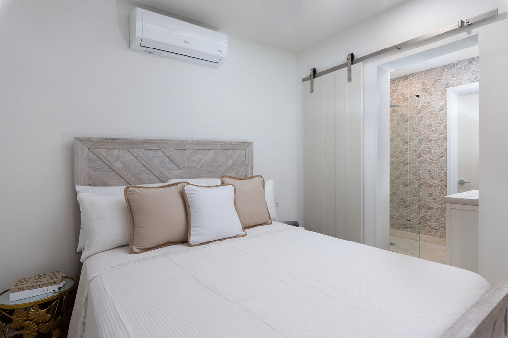 Bedroom with upholstered headboard and en-suite at Calico, a beachfront villa in St James, Barbados